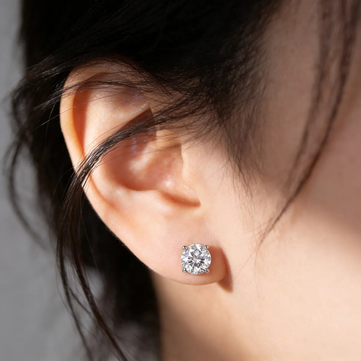 Round cut moissanite stud earrings in four-prong sterling silver setting, 6.5mm hypoallergenic design.